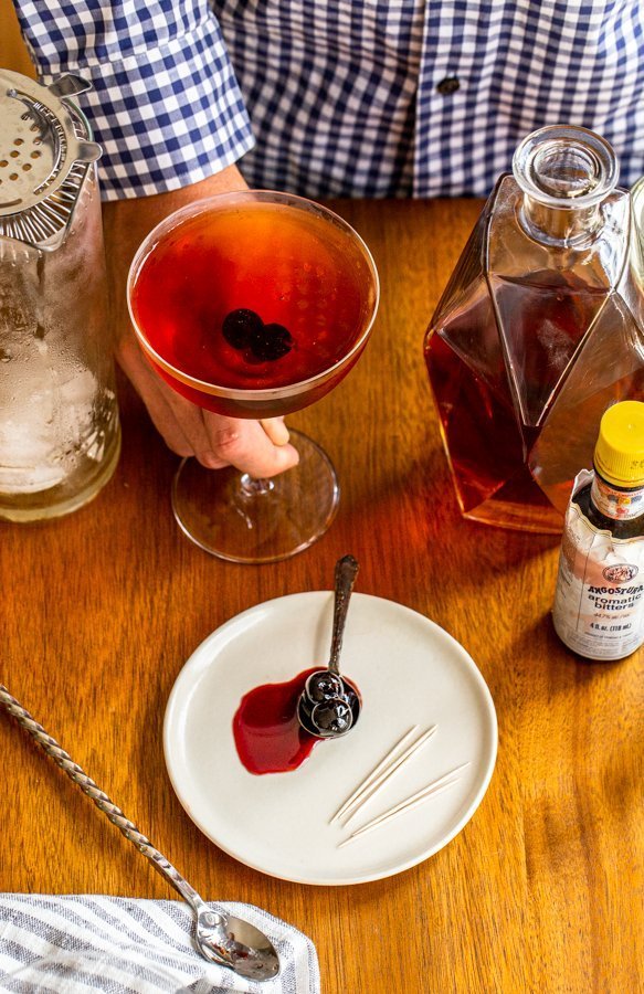 manhattan drink cocktail with cherries in a coupe glass on a wood table