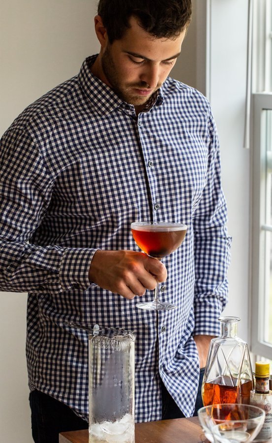 man holding a drink by a window in a blue check shirt