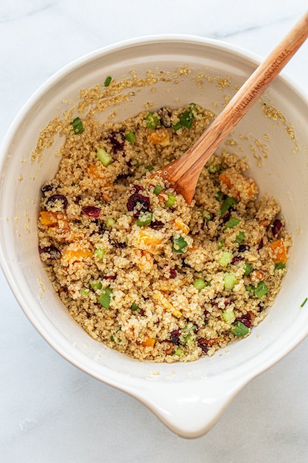 quinoa, cranberries, walnuts, green onions and oranges being mixed in a bowl