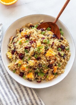 orange cranberry quinoa salad in a white bowl with a wood spoon