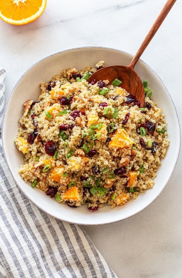 orange cranberry quinoa salad in a white bowl with a wood spoon