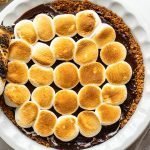s'mores pie with toasted marshmallows in a white pie dish on a white marble counter