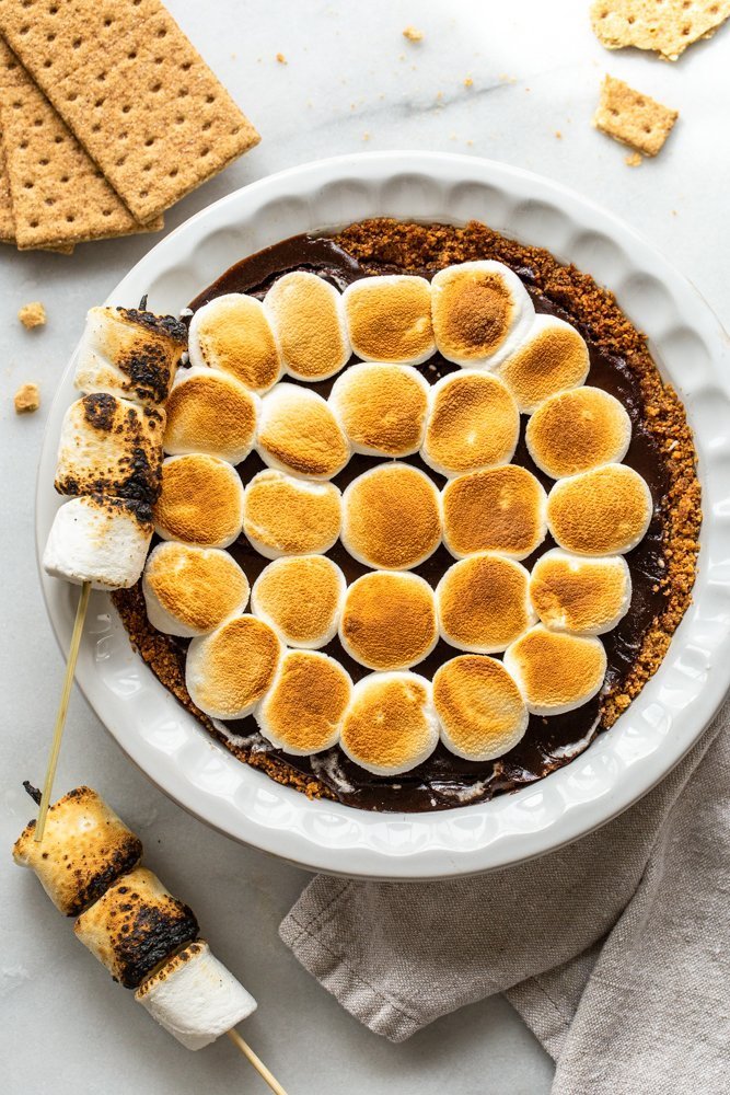 s'mores pie with toasted marshmallows in a white pie dish on a white marble counter