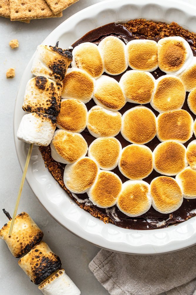 s'mores pie with toasted marshmallows in a white pie dish on a white marble counter