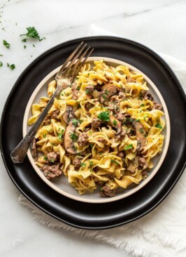 venison stroganoff on a plate with a black charger and a silver fork and parsley