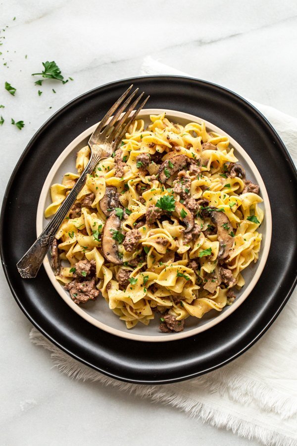 venison stroganoff on a plate with a black charger and a silver fork and parsley