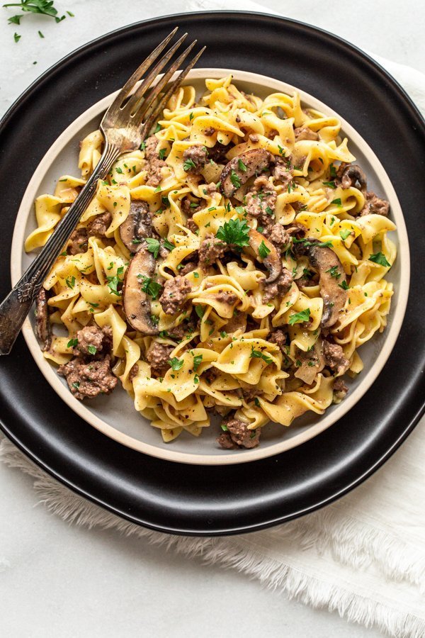 venison stroganoff on a plate with a black charger and a silver fork and parsley