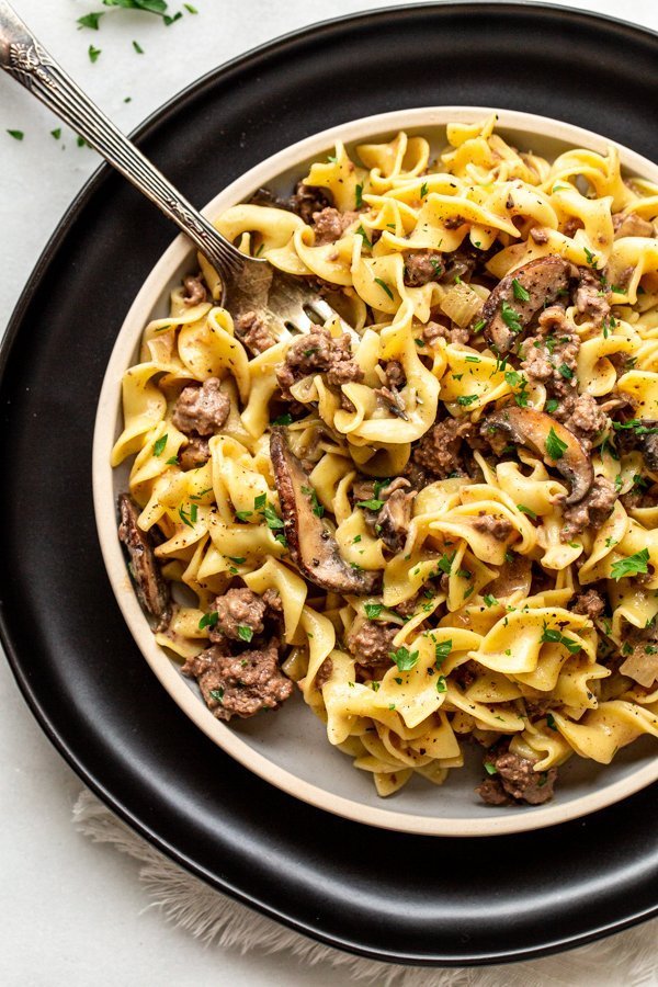 venison stroganoff on a plate with a black charger and a silver fork and parsley