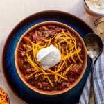 beer chili with cheese and sour cream in an orange bowl in a blue plate