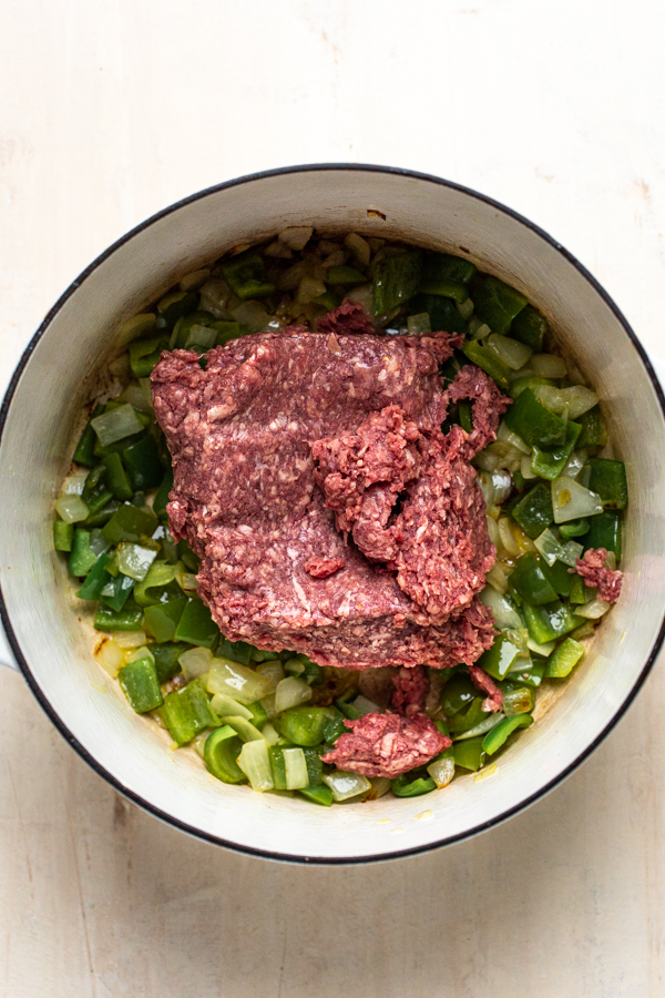 ground meat on top of peppers and onions in a pot