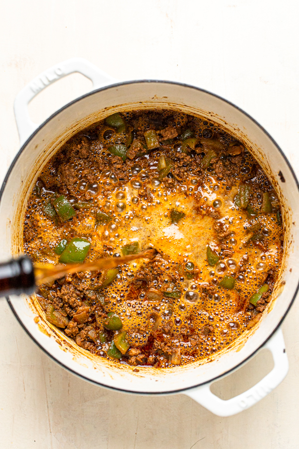 beer being poured into a pot of chili