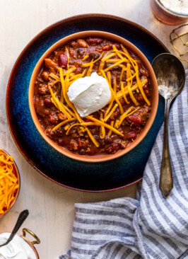 chili with cheese and sour cream in an orange bowl in a blue plate