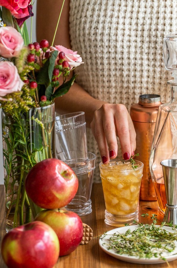 apple cider bourbon smash on a wood board with roses and apples and thyme