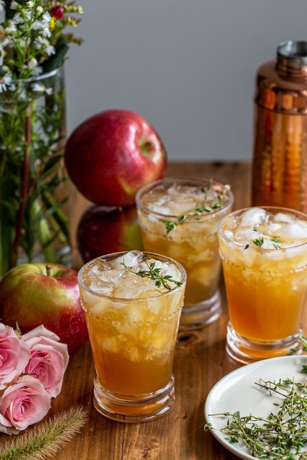 apple cider bourbon smash on a wood board with roses and apples and thyme