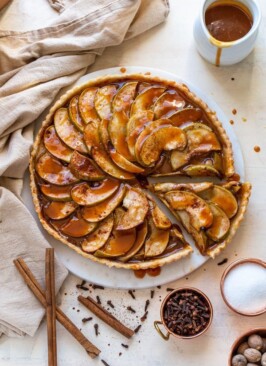 caramel apple tart with a slice cut out of it with cinnamon, cloves and nutmeg