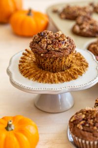 gluten-free pumpkin muffin on a white mini cake sand with pumpkins in the background