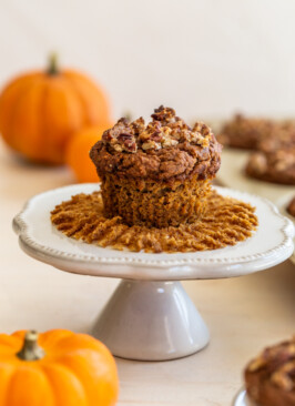 gluten-free pumpkin muffin on a white mini cake sand with pumpkins in the background