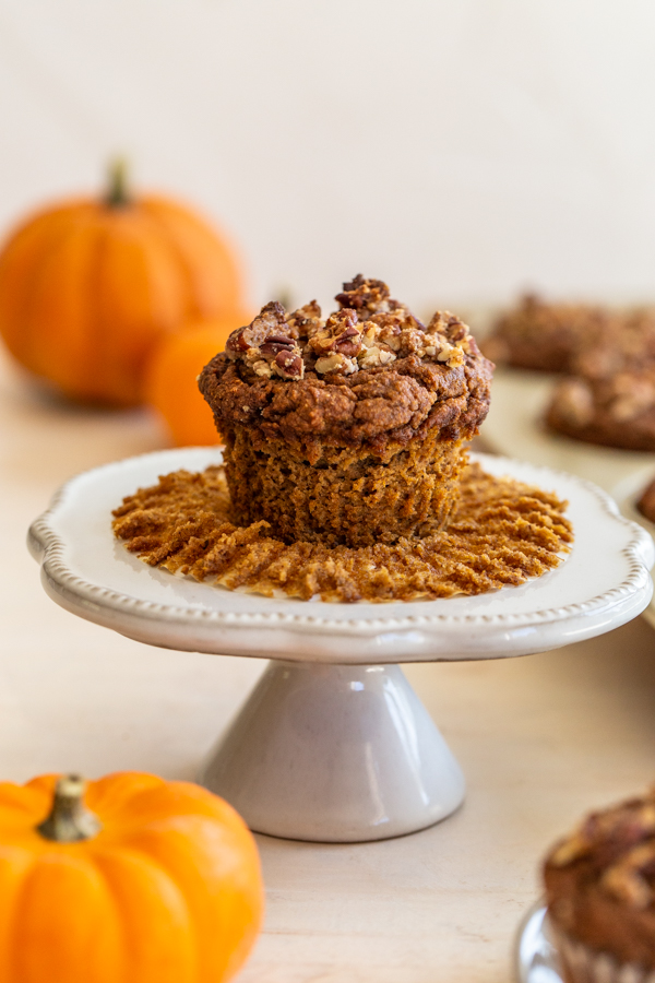 gluten-free pumpkin muffin on a white mini cake sand with pumpkins in the background