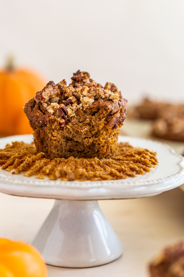 gluten-free pumpkin muffin on a white mini cake sand with pumpkins in the background