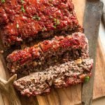 sliced smokey venison meatloaf on a wood platter with a knife