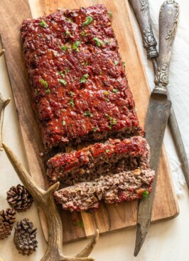 sliced smokey venison meatloaf on a wood platter with a knife