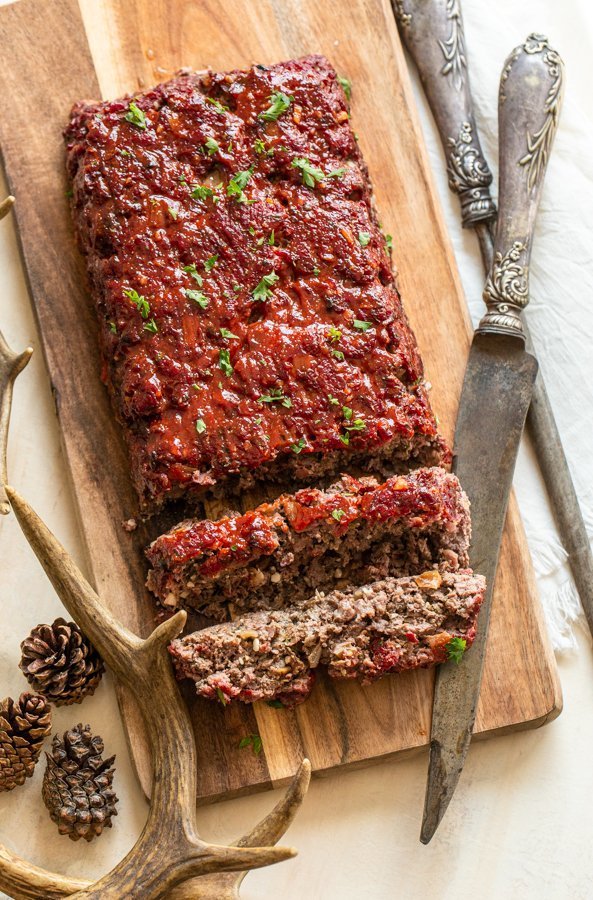 sliced smokey venison meatloaf on a wood platter with a knife