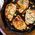 pork chops in a skillet with garlic on a wood table