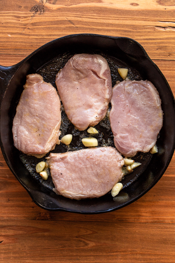 uncooked pork chops in a skillet with garlic