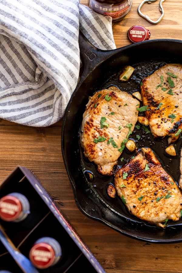 pork chops in a skillet with garlic and hard apple cider