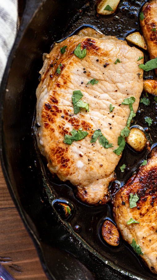 pork chops in a skillet with garlic on a wood table