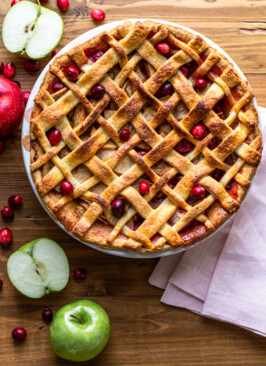 apple cranberry pie on a wood board with a pink napkin, apples and cranberries