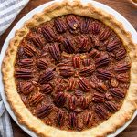 white pie dish filled with pie and pecans with a blue and white striped linen