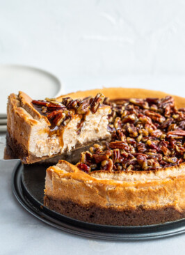 A slice of pecan pie cheesecake being cut out of a big, round cheesecake