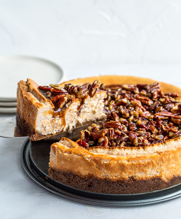 A slice of pecan pie cheesecake being cut out of a big, round cheesecake