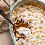 sweet potato casserole with marshmallows and pecans in a blue oval casserole dish with a serving spoon