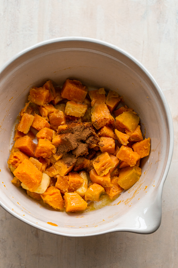 cooked sweet potatoes in a bowl with butter, cinnamon, maple and milk