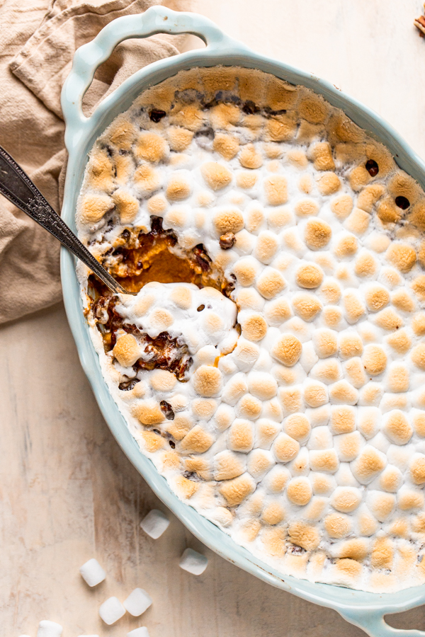 sweet potato casserole with marshmallows and pecans in a blue oval casserole dish with a serving spoon