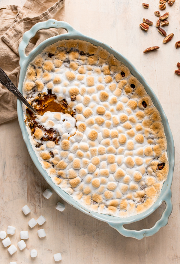 sweet potato casserole with marshmallows and pecans in a blue oval casserole dish with a serving spoon