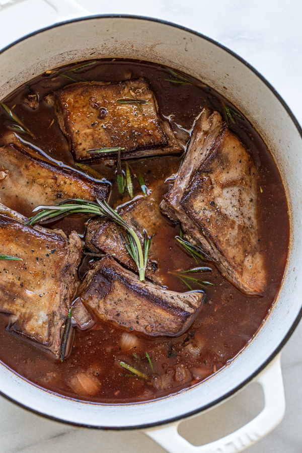 venison short ribs in braising liquid with rosemary sprigs