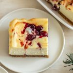 cranberry cheesecake bar on a white plate with greenery