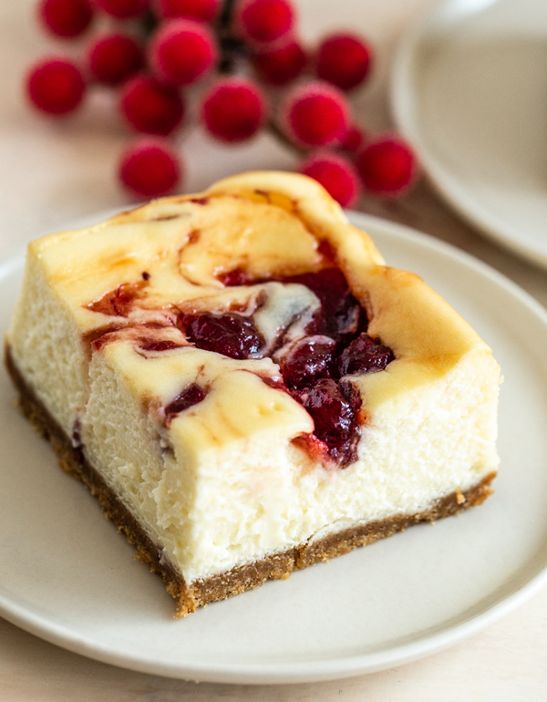 cranberry cheesecake bar on a white plate with greenery