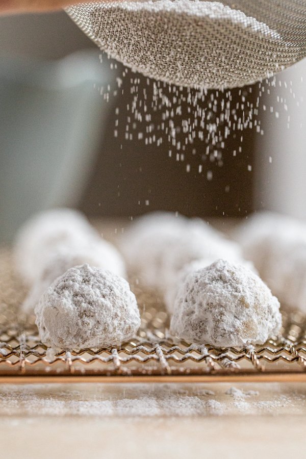 sprinkling powdered sugar over mexican wedding cookies