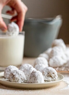 mexican wedding cookies on a plate with one being dunked into a glass of milk