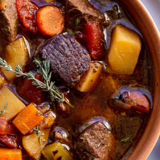 venison stew in a terra-cotta bowl with a thyme leaf