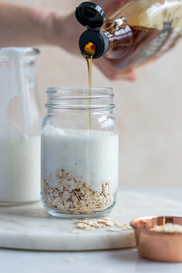maple syrup being poured into a jar with oats and kefir milk