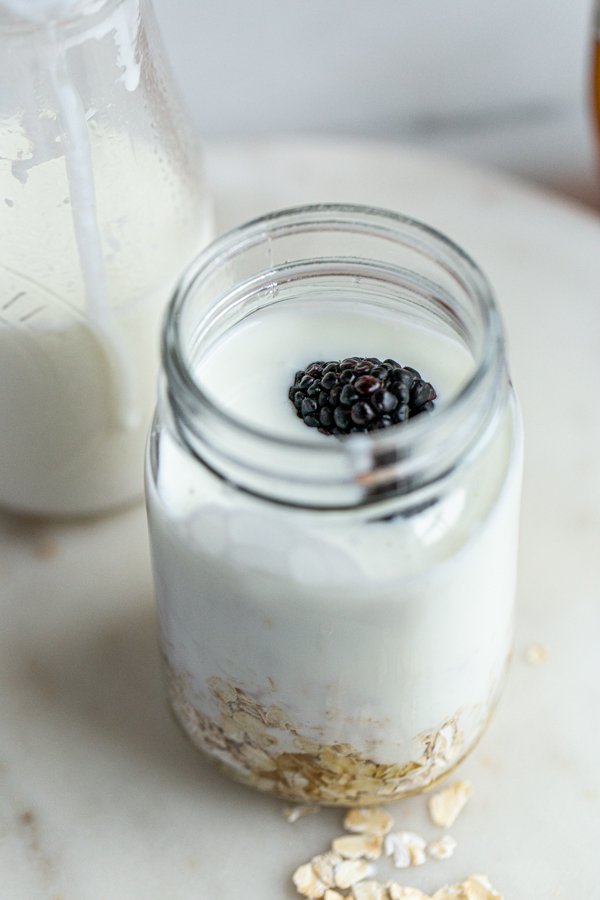 a blackberry on top of a jar with oats and milk inside