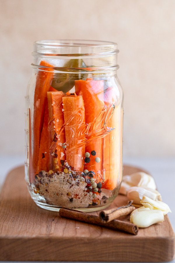 spicy fermented carrots in a glass jar with garlic and cinnamon sticks
