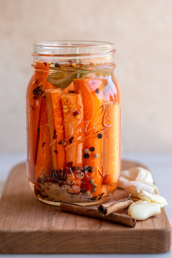 spicy fermented carrots in a glass jar with garlic and cinnamon sticks