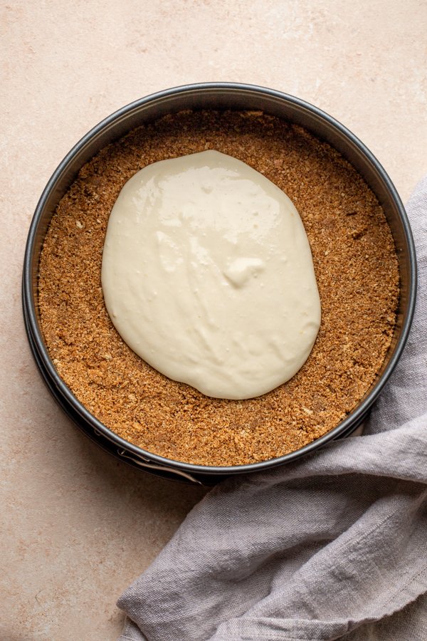 cheesecake being poured over graham cracker crust