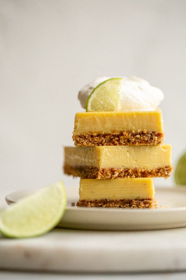 key lime pie bars stacked with fresh whipped cream and a lime